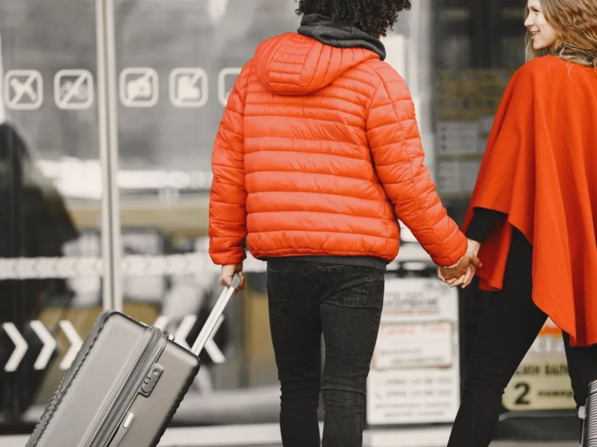Ein Paar geht Hand in Hand mit einem Rollkoffer zum Terminal, Symbolbild für die Abreise in die Flitterwochen