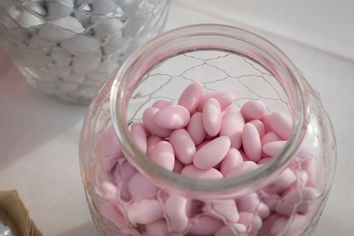 Offenes Glasgefäß voller rosafarbener Zuckermandeln, dahinter ein zweites Glas mit weißen Zuckermandeln