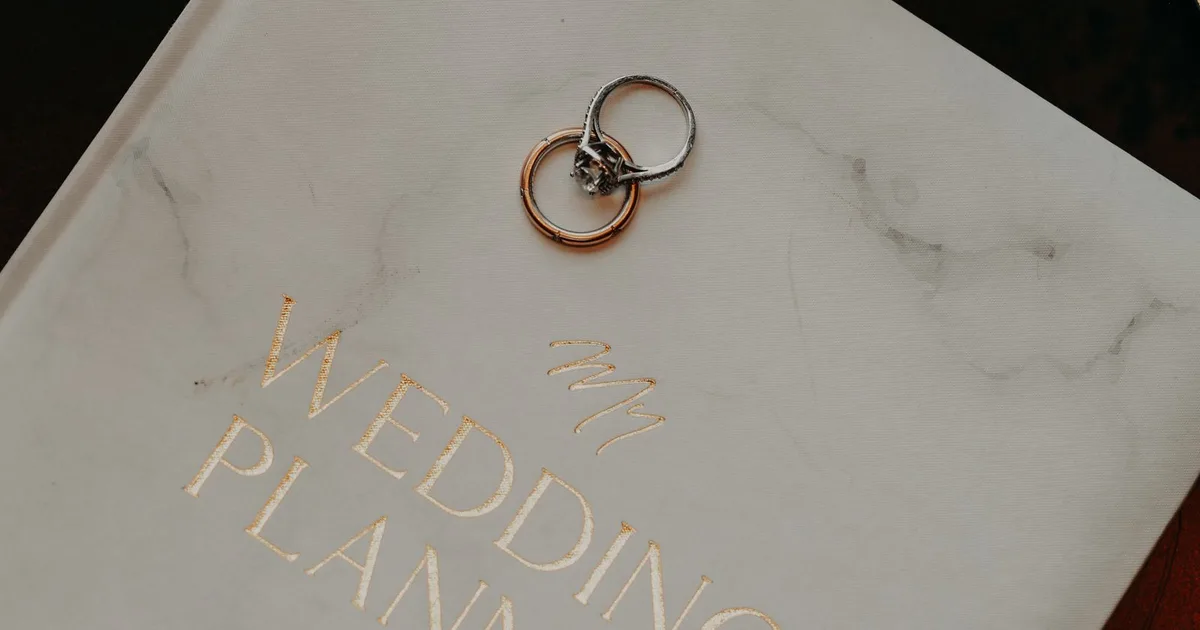 Zwei Eheringe auf einem Hochzeitsplaner-Buch als Symbol für die geplante Hochzeit
