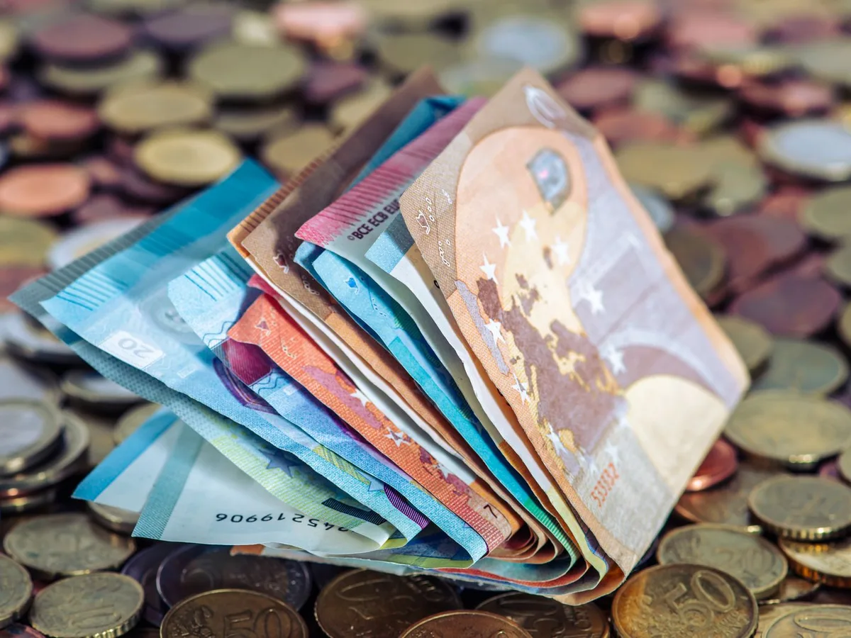 Gefächerte Euro-Geldscheine stehen aufrecht auf einem Haufen Euro-Münzen