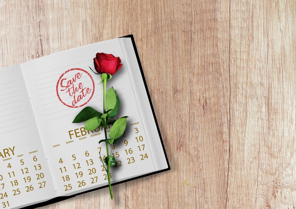 Ein Kalender auf dem eine Rose liegt und ein roter Stempel mit 'Save-the-Date'
