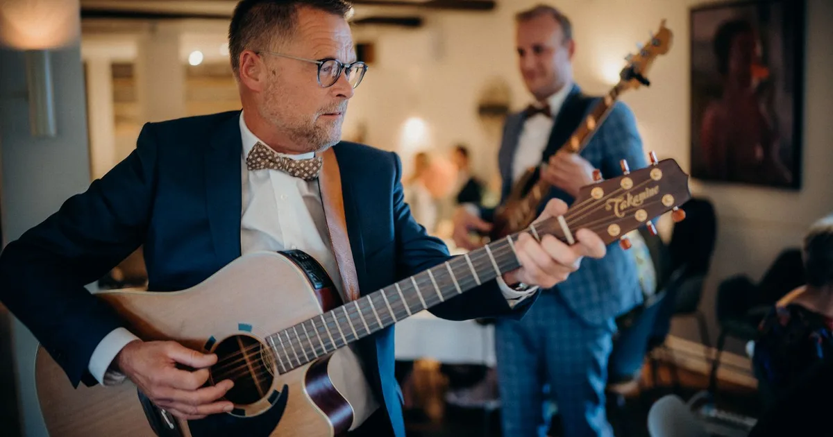 Zwei Musiker im Anzug spielen Akustikgitarre und Bass bei einer Hochzeitsfeier im Saal