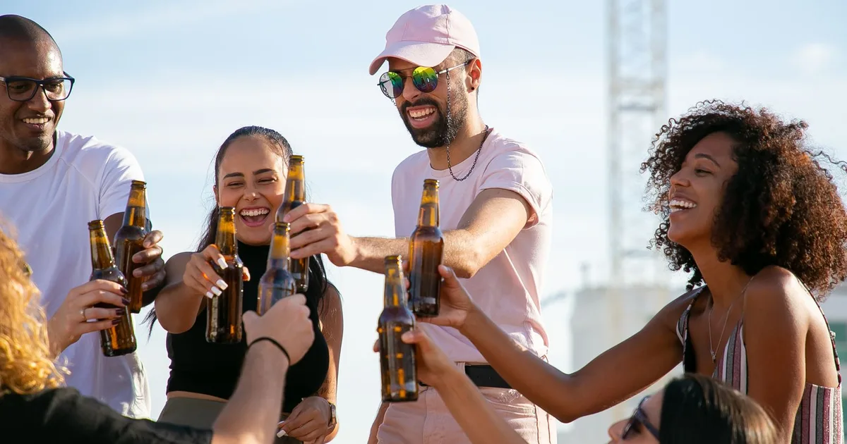 Gemischte Gruppe von Freunden stößt bei einer Feier im Freien mit Bierflaschen an