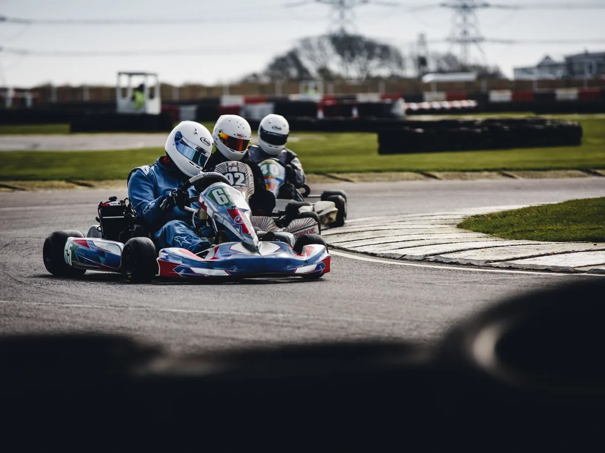 Drei Kartfahrer in Helm und Rennanzug auf einer Kart-Rennstrecke in einer Kurve