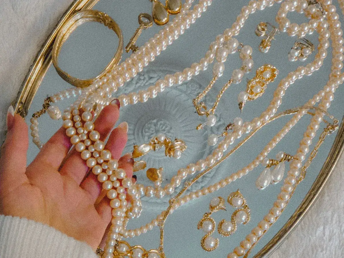 Eine Hand hält mehrere Perlenketten über einem Tablett mit weiterem Perlenschmuck