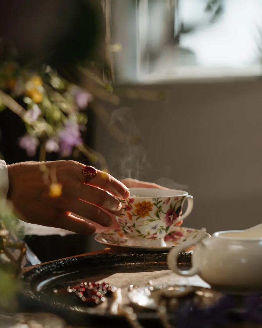 Hand greift nach einer blumig bemalten Porzellan-Teetasse auf einer Untertasse