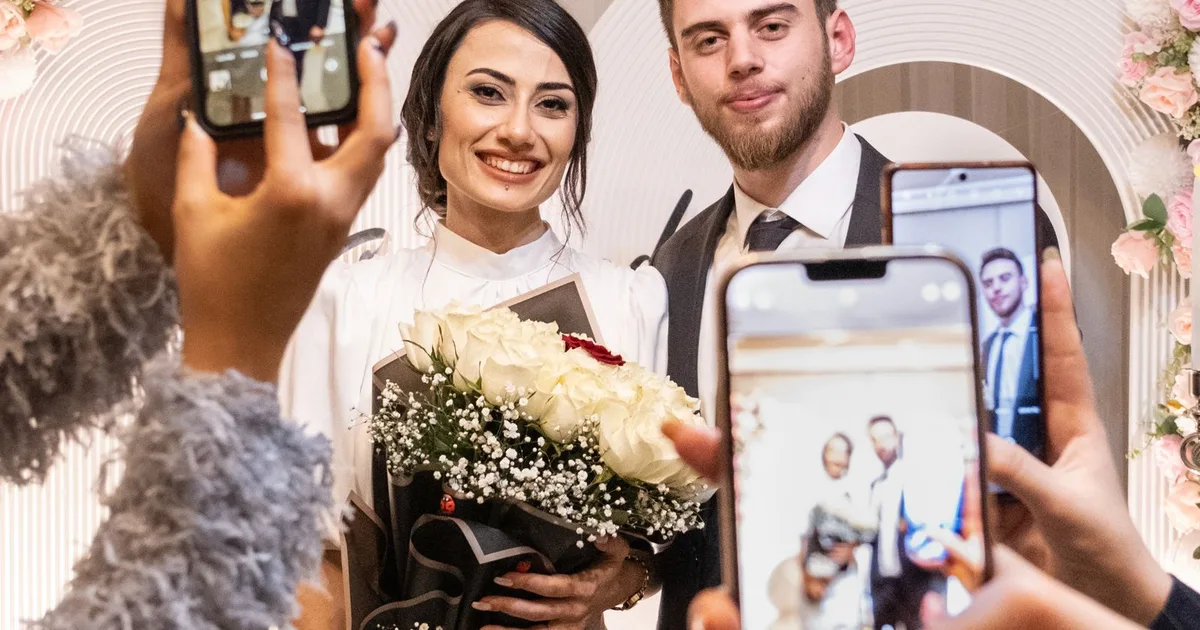 Hochzeitsgäste fotografieren das lächelnde Brautpaar mit ihren Smartphones