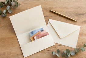 Geöffnete Glückwunschkarte mit eingelegten Euro-Scheinen und einem Umschlag auf einem Eichentisch