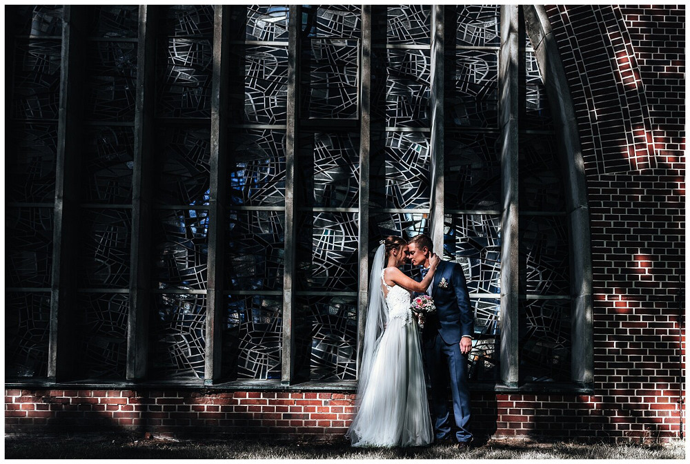 Ein Brautpaar küsst sich vor dem Mosaikfenster einer Kirche