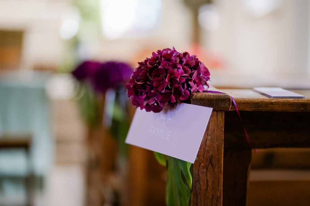 Purpurne Blume hängt an einer Kirchenbank und ein Glückwunschumschlag ist daran befestigt