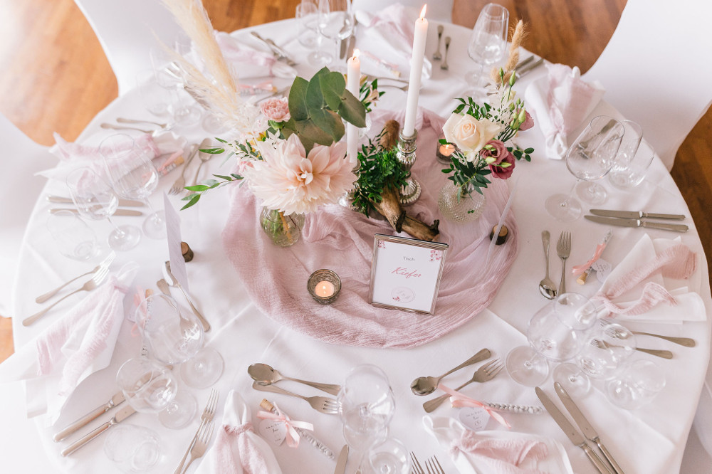 Eine runde Hochzeitstafel mit Geschirr, Floristik und Papeterie