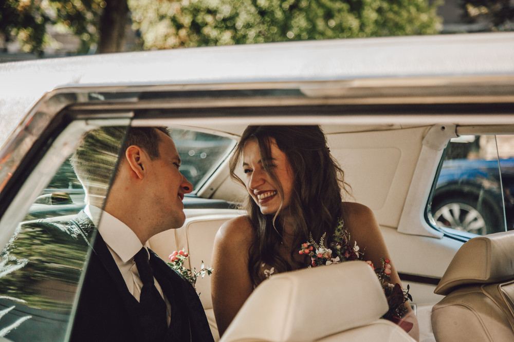 Traupaar sitzt im Hochzeitsfahrzeug und die Braut hält den Brautstrauß