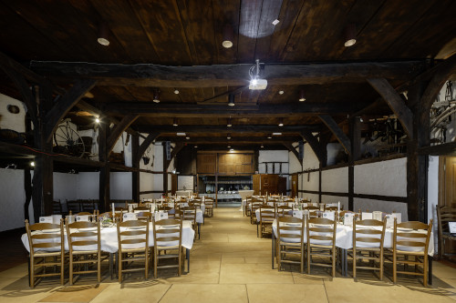 In der Deele stehen gedeckte Tische für die Gäste während der Hochzeit; oben an der Decke sind kräftige Querbalken; links und rechts befinden sich die zweistöckigen Seitenschiffe