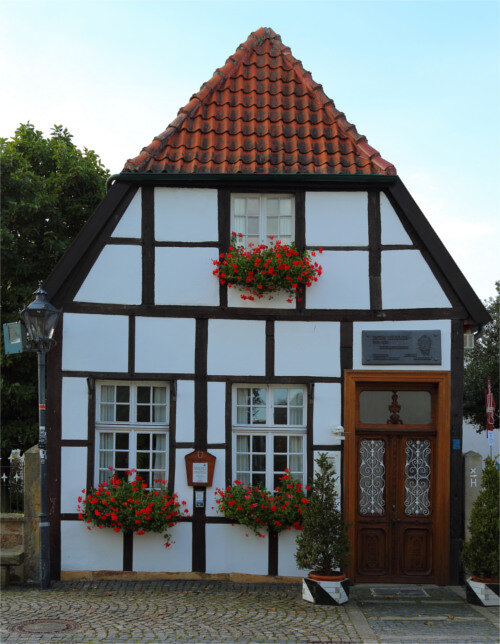 Heimathaus Bevergern: Fachwerkhaus mit weißen Scheunenfenstern, die mit Blumenkästen geschmückt sind