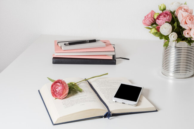 Ein Blumenstrauß steht auf dem Tisch und eine einzelne Rose liegt auf einem Buch. Dahinter sind mehrere Notizblöcke gestapelt zur Hochzeitsvorbereitung